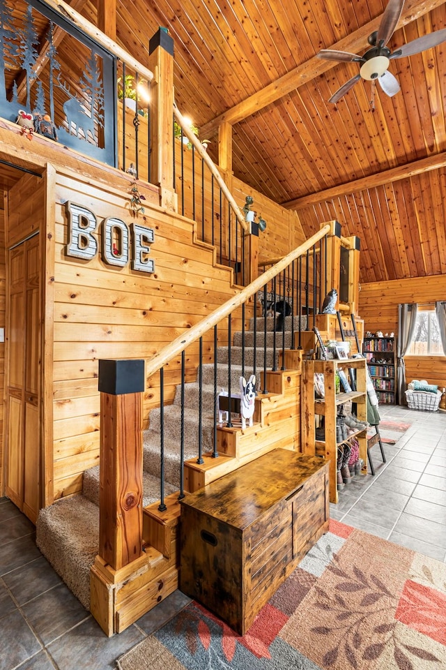 stairway with tile patterned floors, wood walls, lofted ceiling with beams, wooden ceiling, and ceiling fan