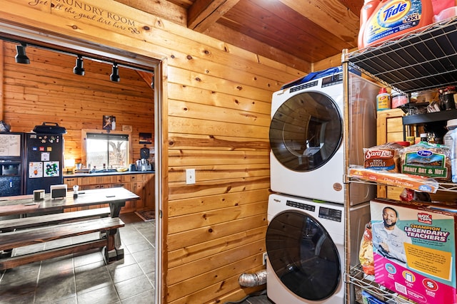 washroom featuring stacked washer and clothes dryer, dark tile patterned flooring, wood ceiling, and wood walls