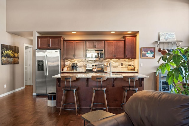 kitchen featuring appliances with stainless steel finishes, a kitchen breakfast bar, dark hardwood / wood-style floors, light stone counters, and tasteful backsplash