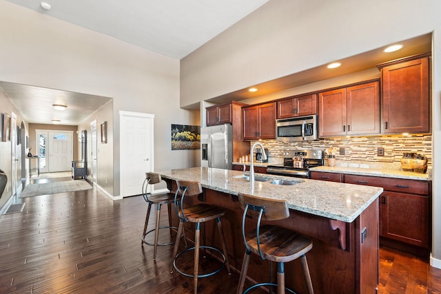 kitchen featuring light stone counters, sink, stainless steel appliances, and an island with sink