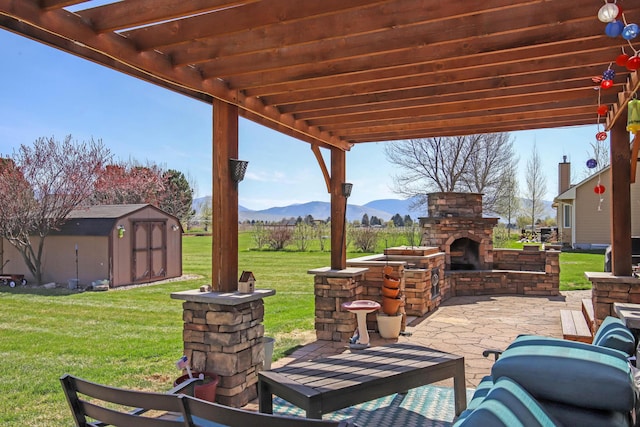 view of patio / terrace featuring a mountain view, a shed, an outdoor stone fireplace, and a pergola