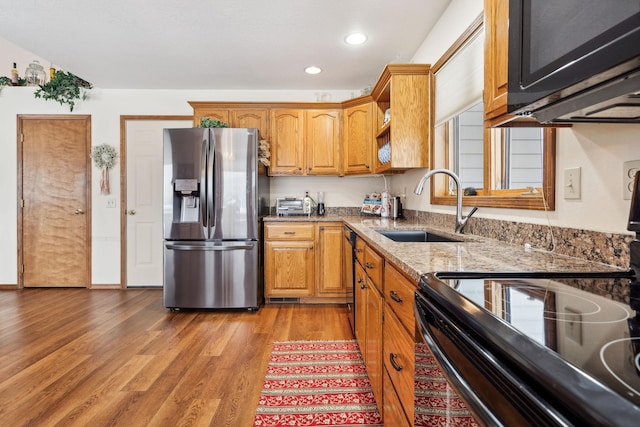 kitchen with range with electric cooktop, sink, stainless steel fridge, hardwood / wood-style flooring, and light stone counters