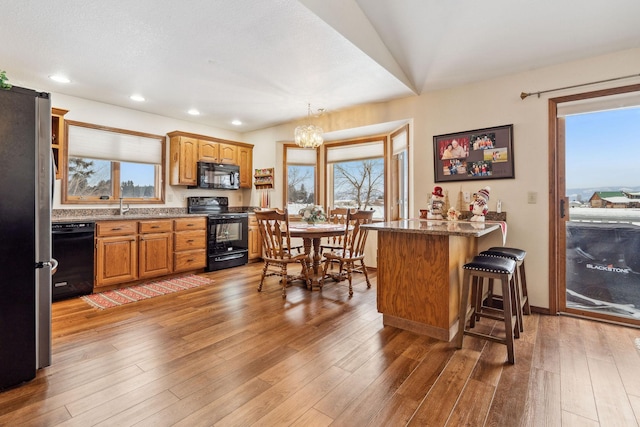 kitchen featuring hardwood / wood-style floors, plenty of natural light, black appliances, and a kitchen breakfast bar