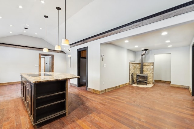 kitchen featuring pendant lighting, light stone counters, an island with sink, vaulted ceiling, and a wood stove