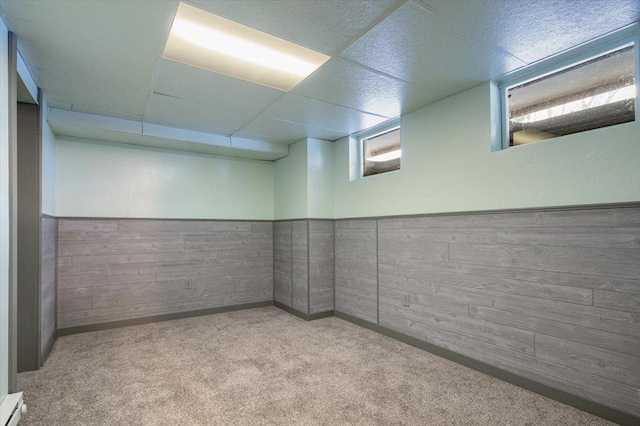 basement with baseboard heating, a paneled ceiling, wooden walls, and light carpet