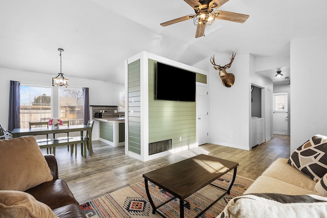 living room featuring ceiling fan with notable chandelier, vaulted ceiling, light hardwood / wood-style floors, and washing machine and clothes dryer