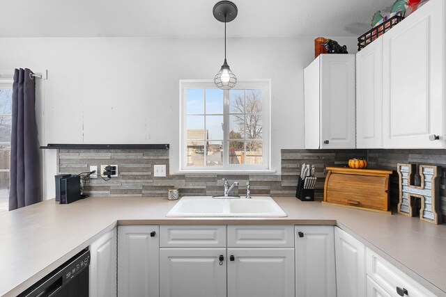 kitchen with light countertops, hanging light fixtures, white cabinets, a sink, and dishwasher