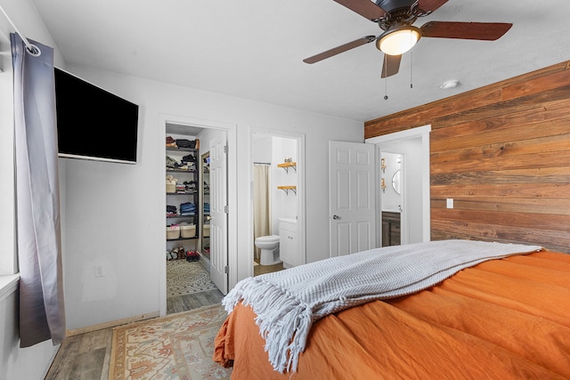 bedroom with wood finished floors, ensuite bath, wood walls, a walk in closet, and a closet