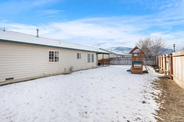 yard covered in snow featuring a playground, a fenced backyard, and a mountain view