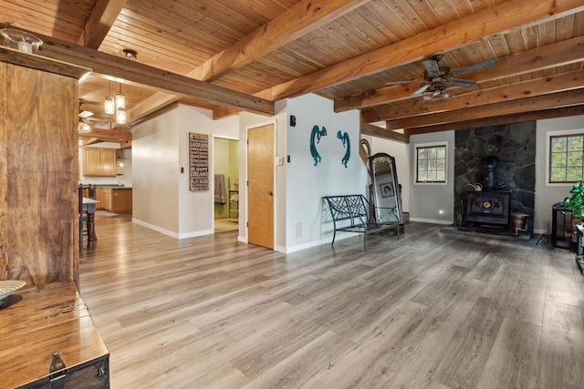 unfurnished living room featuring beam ceiling, a wood stove, wood ceiling, and light hardwood / wood-style floors