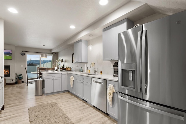 kitchen featuring sink, hanging light fixtures, kitchen peninsula, stainless steel appliances, and light hardwood / wood-style flooring