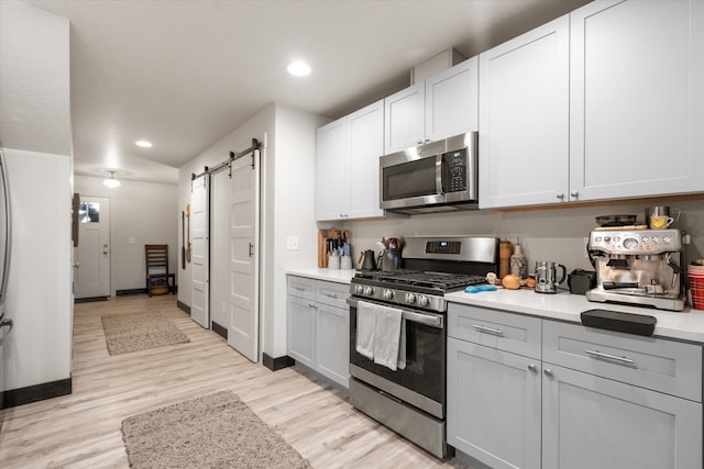 kitchen featuring gray cabinets, appliances with stainless steel finishes, white cabinetry, a barn door, and light wood-type flooring