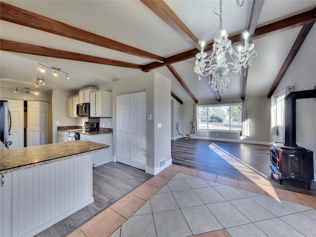 kitchen featuring a chandelier, a wood stove, light tile patterned floors, pendant lighting, and stainless steel appliances