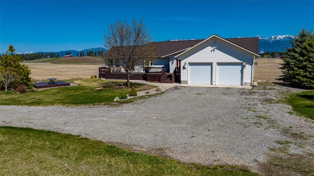 single story home with a garage, a deck with mountain view, and a front lawn