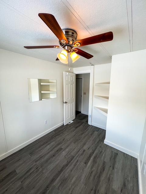 unfurnished bedroom with a textured ceiling, dark wood-type flooring, and ceiling fan