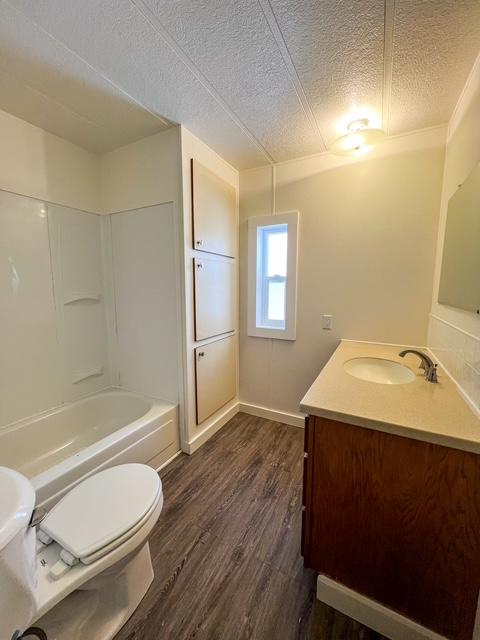 full bathroom with hardwood / wood-style flooring, vanity, a textured ceiling, shower / washtub combination, and toilet