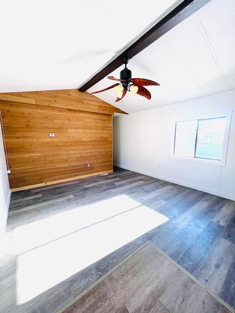 bonus room featuring dark hardwood / wood-style flooring, vaulted ceiling with beams, wooden walls, and ceiling fan