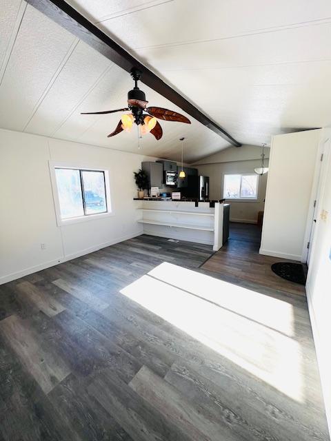 unfurnished living room featuring ceiling fan, plenty of natural light, dark hardwood / wood-style floors, and vaulted ceiling with beams