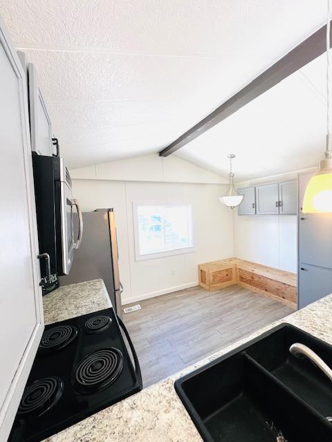 kitchen featuring pendant lighting, lofted ceiling with beams, sink, light hardwood / wood-style floors, and stainless steel appliances