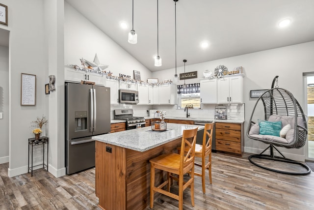 kitchen with hanging light fixtures, stainless steel appliances, light stone counters, white cabinets, and a kitchen island