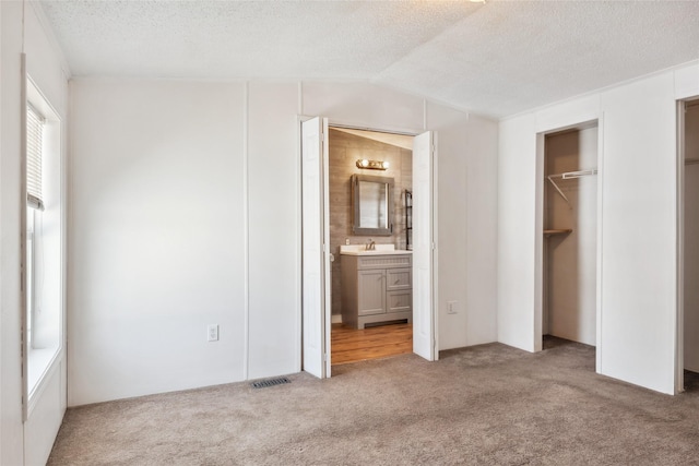 unfurnished bedroom with light carpet, connected bathroom, lofted ceiling, and a textured ceiling