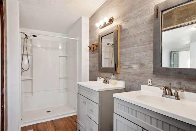 bathroom featuring wooden walls, a shower, wood-type flooring, vanity, and a textured ceiling