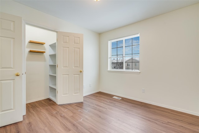 unfurnished bedroom featuring lofted ceiling, a spacious closet, and light hardwood / wood-style flooring