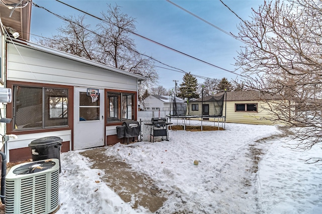 yard covered in snow featuring central AC unit and a trampoline