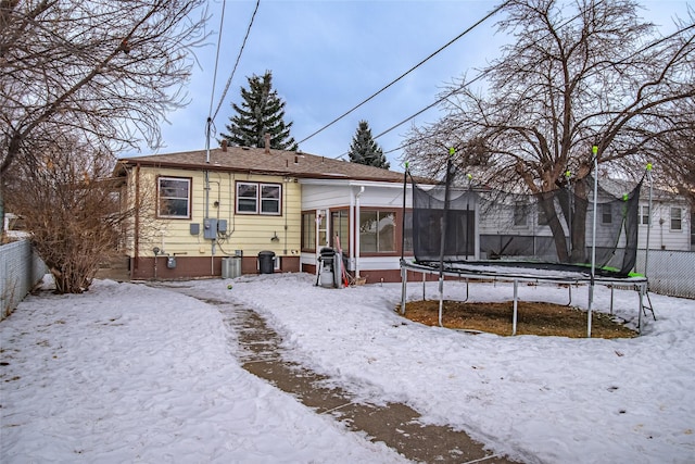 snow covered house with central AC, a sunroom, and a trampoline