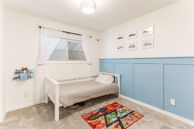 bedroom with wainscoting, carpet, and a decorative wall