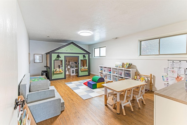 recreation room with baseboards, light wood-style flooring, visible vents, and a textured ceiling