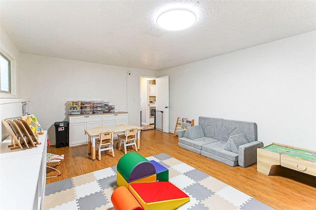 recreation room featuring a textured ceiling, light wood-type flooring, and washer / dryer