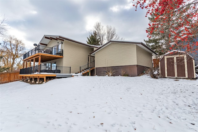 snow covered property featuring an outdoor structure, fence, a balcony, and a shed