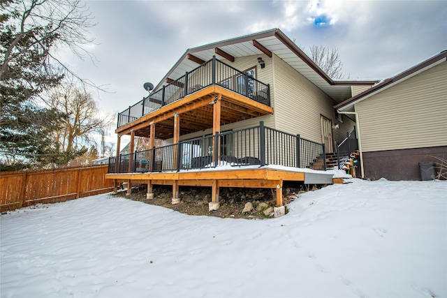 snow covered back of property featuring fence and a wooden deck