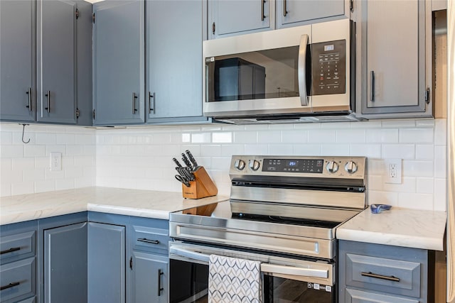 137 Cascade St, Lolo, MT 59847 - kitchen with appliances with stainless steel finishes, tasteful backsplash, light stone countertops, and blue cabinetry