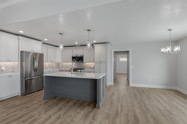 kitchen featuring hanging light fixtures, stainless steel appliances, white cabinets, and light wood-type flooring