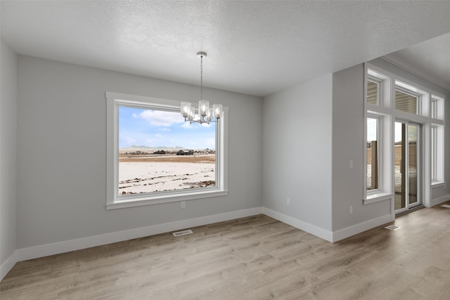 unfurnished dining area featuring a notable chandelier, a textured ceiling, and light hardwood / wood-style flooring