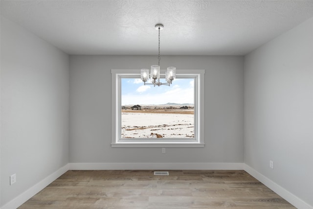 unfurnished room featuring a healthy amount of sunlight, a notable chandelier, and light hardwood / wood-style floors