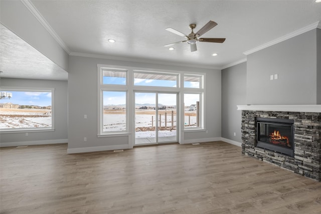 unfurnished living room featuring ceiling fan, a stone fireplace, light hardwood / wood-style flooring, and a textured ceiling