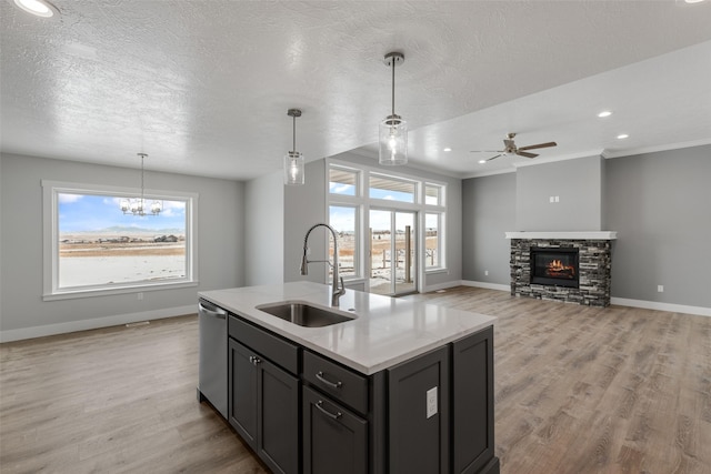 kitchen with sink, light hardwood / wood-style flooring, dishwasher, an island with sink, and pendant lighting