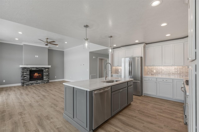 kitchen with sink, appliances with stainless steel finishes, hanging light fixtures, an island with sink, and white cabinets