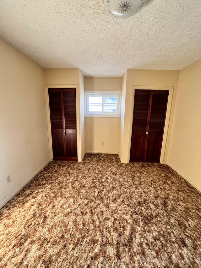 unfurnished bedroom featuring two closets, carpet floors, and a textured ceiling