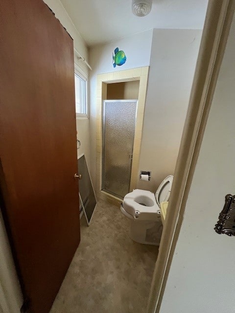 bathroom featuring a shower with door and toilet