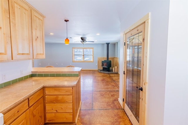 kitchen featuring pendant lighting, a ceiling fan, open floor plan, a peninsula, and a wood stove