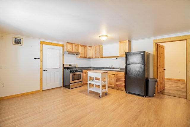 kitchen with under cabinet range hood, a sink, dark countertops, freestanding refrigerator, and stainless steel range with gas stovetop