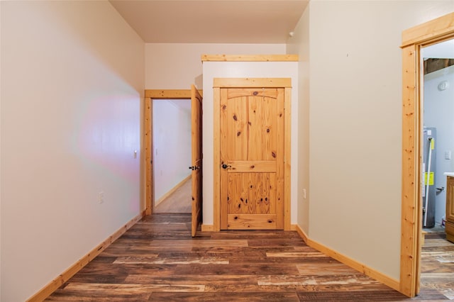 hallway featuring wood finished floors, water heater, and baseboards