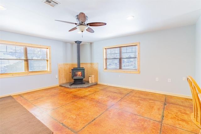 unfurnished living room with visible vents, plenty of natural light, baseboards, and a wood stove