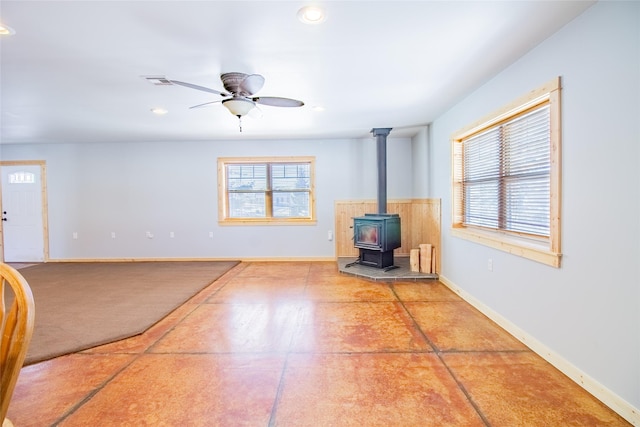 unfurnished living room with visible vents, ceiling fan, a wood stove, and baseboards