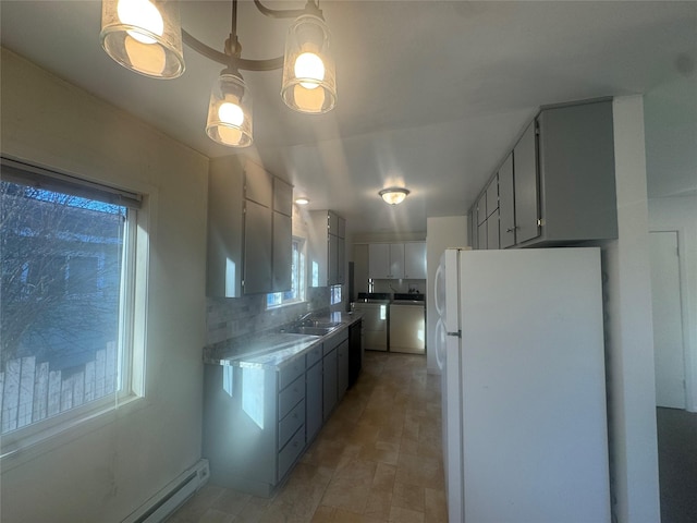 kitchen featuring a baseboard heating unit, a wealth of natural light, washing machine and clothes dryer, and white fridge