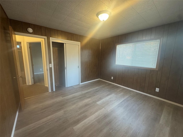 unfurnished bedroom with hardwood / wood-style flooring, wooden walls, and a closet